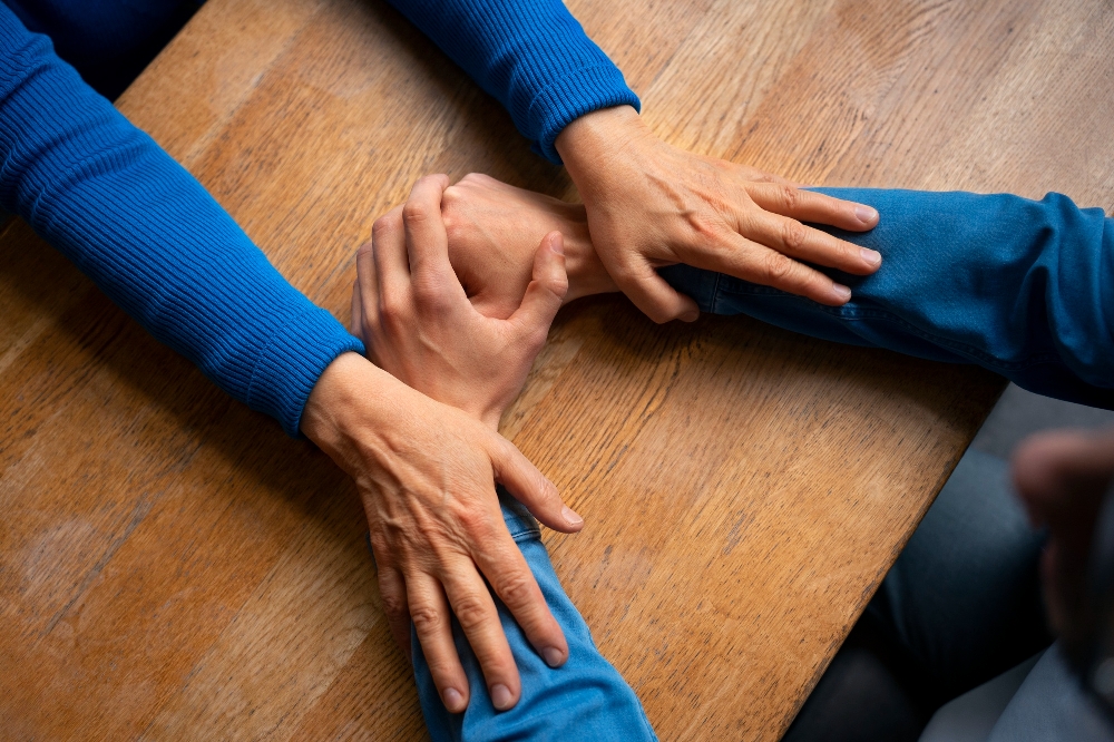 Two people clasp hands together on wooden table.